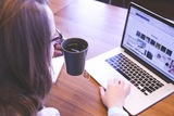 een vrouw met bril en koffie in haar linkerhand zoekt wat informatie op haar laptop